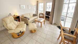 A spacious living room with a beige sofa, a wooden coffee table, and a TV on a stand.