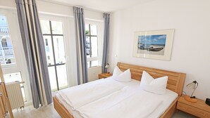 A neatly made bed with white linens and pillows, a wooden headboard, a bedside table with a lamp, and a framed picture on the wall.