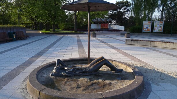 A public square with a central sculpture of a reclining figure, benches, and informational boards. - House Lachmöwe Karl Hagen on Usedom - House Lachmöwe (Karlshagen)
