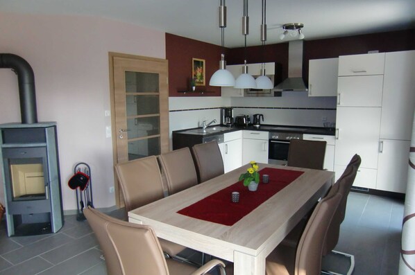 Una cocina moderna con armarios blancos, horno empotrado y una zona de comedor con mesa y sillas de madera.