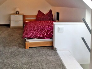 A bedroom with a bed, a nightstand, a lamp, and a white wall. - Le Papillon apartment rental - Apartment (Kröslin)