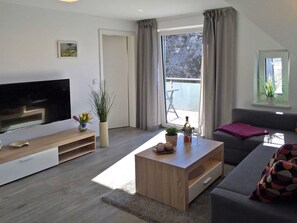 A modern living room with a flat-screen TV, a wooden coffee table, a grey sofa, and a balcony with a table and chairs. - Le Papillon apartment rental - Apartment (Kröslin)