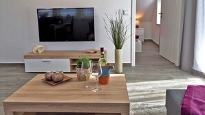 A modern living room with a flat-screen TV, wooden coffee table, decorative plants, and a cozy seating area. - Le Papillon apartment rental - Apartment (Kröslin)