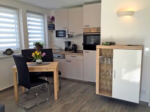 A compact kitchen with a dining area, a microwave, an oven, and a refrigerator. - Le Papillon apartment rental - Apartment (Kröslin)