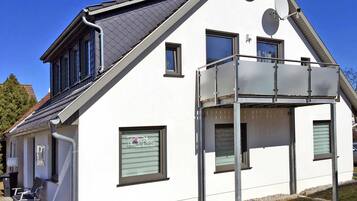 Ein modernes, zweistöckiges Haus mit Balkon, Satellitenschüssel und einem kleinen Fenster mit einem Schild.