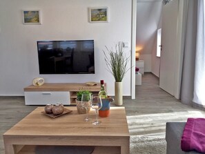 A modern living room with a flat-screen TV, wooden coffee table, decorative plants, and a cozy seating area. - Le Papillon apartment rental - Apartment (Kröslin)