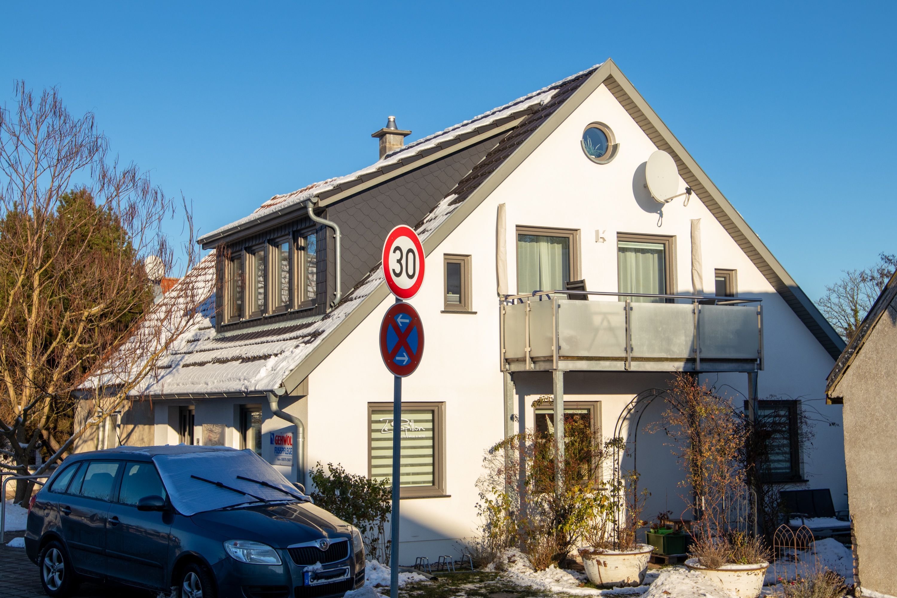 Una casa de dos pisos con techo nevado, una antena parabólica y una señal de límite de velocidad de '30'.
