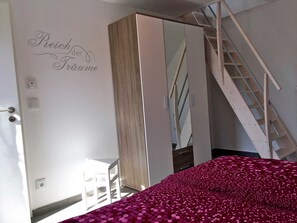 A bedroom with a bed, a wardrobe, a mirror, and a staircase.