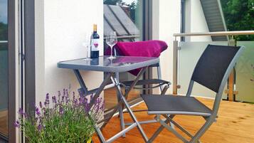 Ein Balkon mit Tisch, Stuhl, einer Weinflasche und einem Blumentopf.