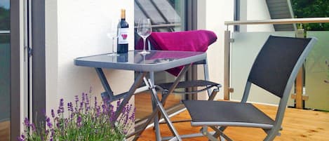 A balcony with a table, a chair, a bottle of wine, and a potted plant.