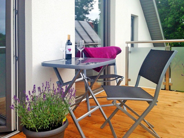 A balcony with a table, a chair, a bottle of wine, and a potted plant.