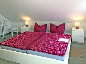 A modern bedroom with a large bed, two nightstands, a small table, and a floor lamp.