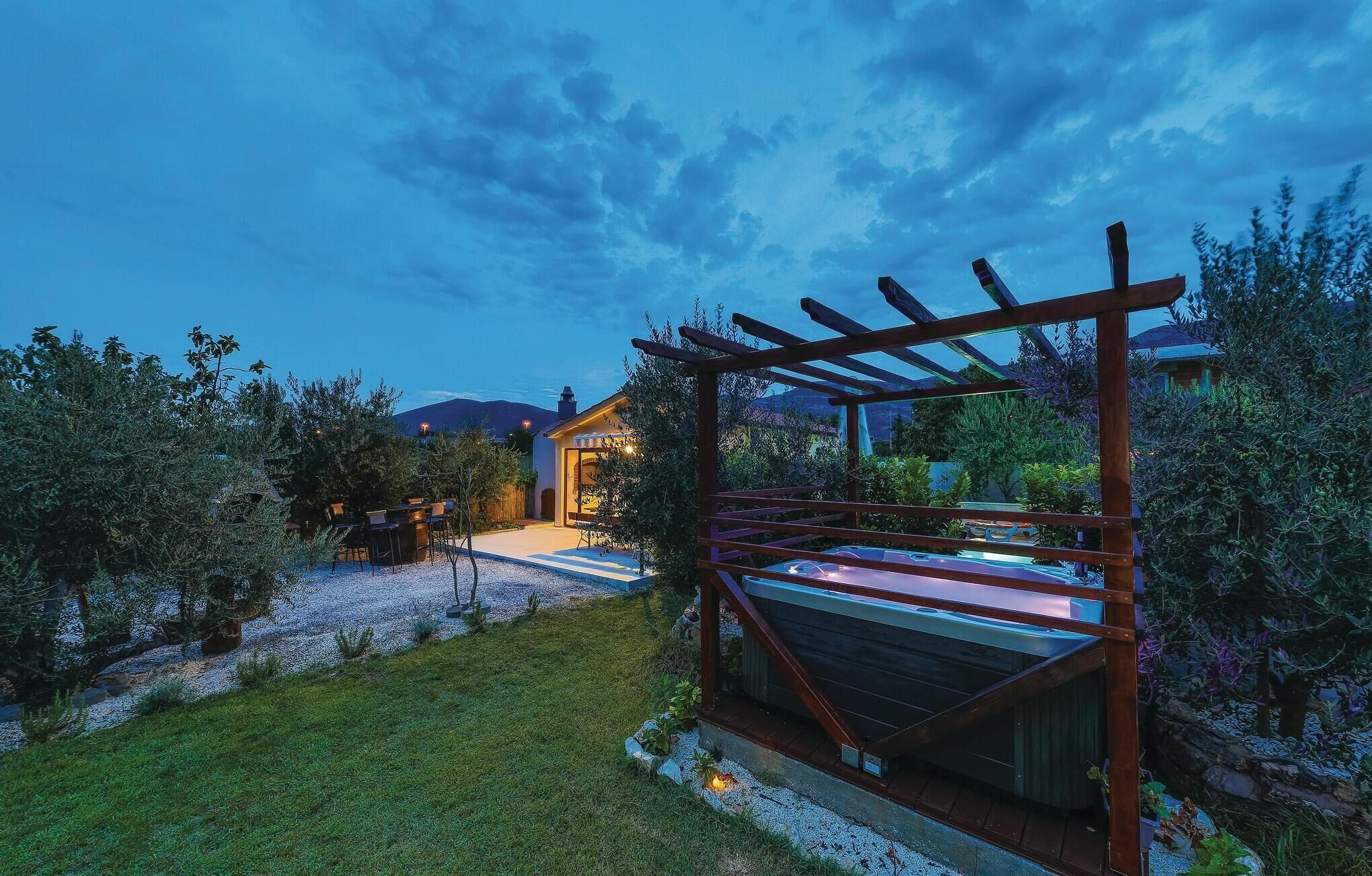 Una pérgola de madera con terraza, rodeada por un jardín ajardinado con diversas plantas y un sendero de grava.
