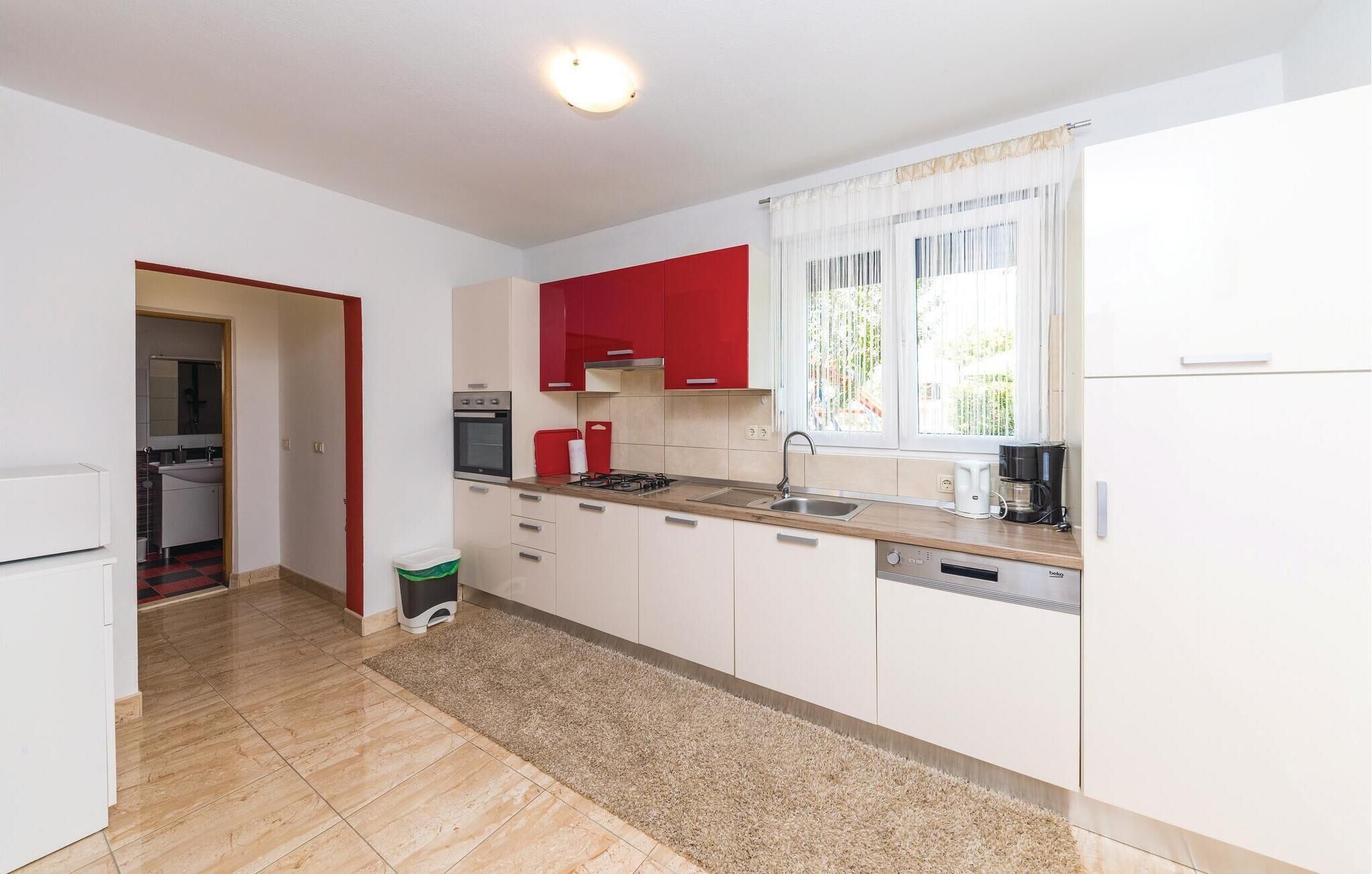 A modern kitchen with white and red cabinets, a built-in oven, a coffee maker, and a window with curtains.