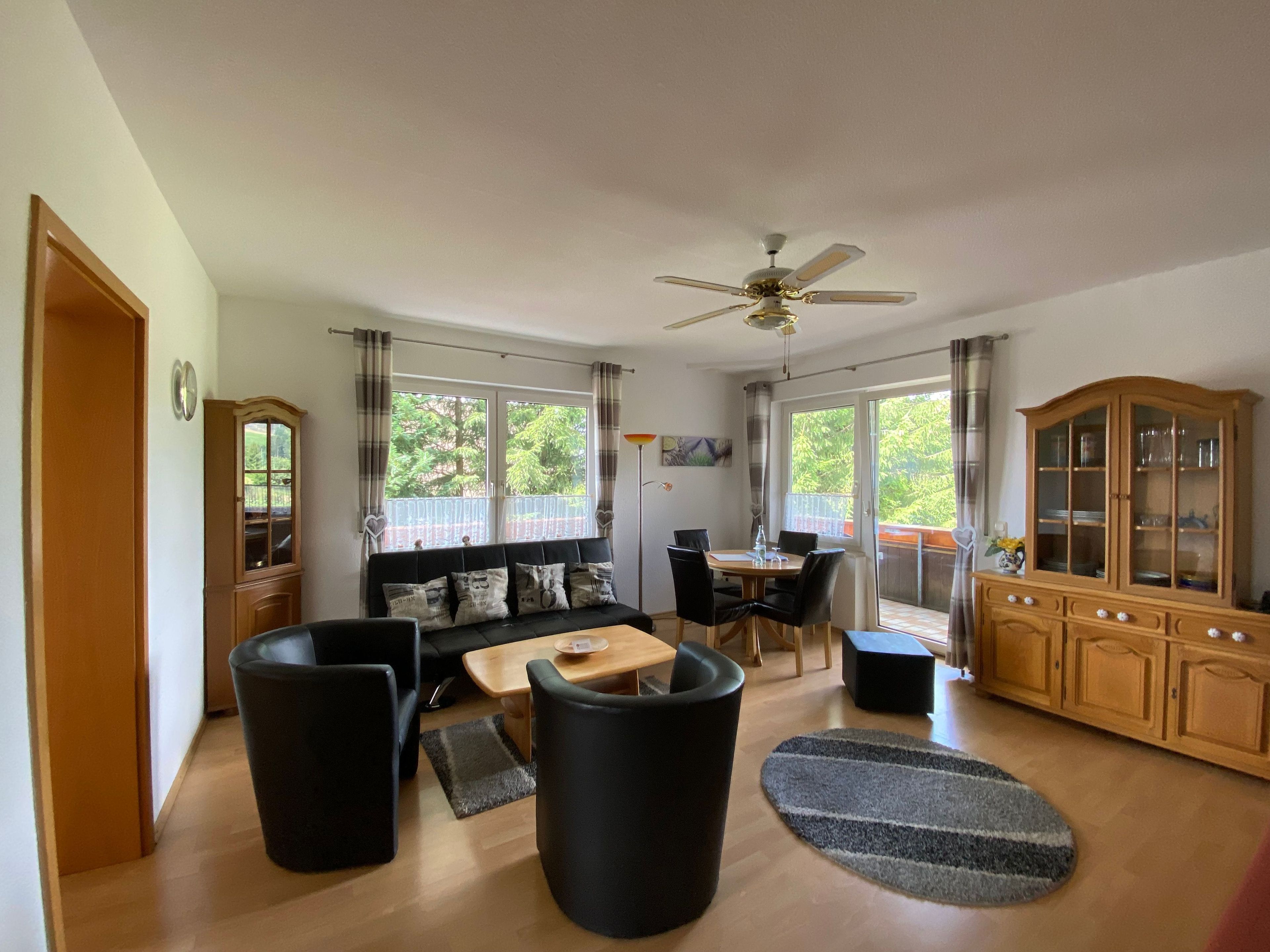 A living room with a sofa, a dining table, a ceiling fan, and a wooden cabinet.