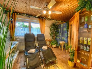Una habitación con dos sillones reclinables, un ventilador de techo, una ventana con cortinas y un armario con botellas.