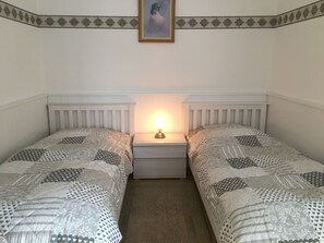 Ein Doppelzimmer mit zwei Betten, einem Nachttisch mit Lampe und einem gerahmten Bild an der Wand.