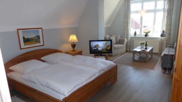 A bedroom with a wooden bed, a television, a chair, and a small table. - (129/8) 1- room apartment balcony - apartment house Plückhahn (Kühlungsborn)