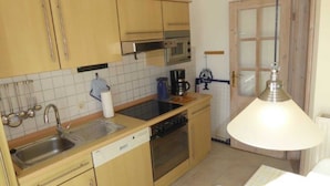 A compact kitchen with wooden cabinets, a dishwasher, a stove, and a coffee maker. - (129/8) 1- room apartment balcony - apartment house Plückhahn (Kühlungsborn)
