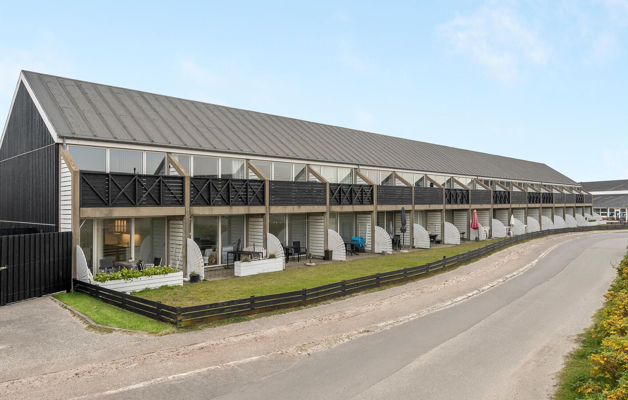 A modern building with a metal roof, large windows, and a covered outdoor seating area with tables and chairs.