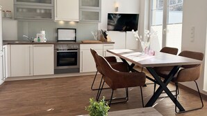 A modern kitchen with white cabinets, a built-in oven, and a dining area with a wooden table and brown chairs.
