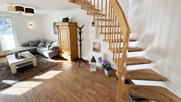 A spacious living room with a wooden staircase, a sofa, a coffee table, and a cabinet.
