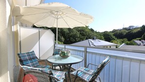 A balcony with a round table, two chairs, a large umbrella, and a wicker chair.
