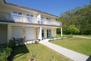 A two-story house with a balcony, a covered patio, and a small garden area.