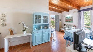 Un espacio habitable compacto con un mueble azul, una mesita de centro blanca, un televisor y una ventana con vistas a zonas verdes.