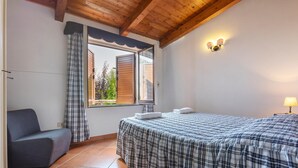 Un dormitorio con cama, una silla, una ventana con cortinas y una lámpara fijada a la pared.