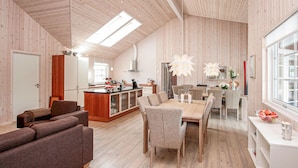 A spacious living area with a wooden ceiling, a dining table with chairs, a kitchen area with a central island, and a large window providing natural light. - Amazing home in Idestrup with sauna (Idestrup)