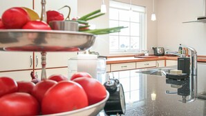 A kitchen with a modern design, featuring a stainless steel sink, a kettle, and a bowl of red tomatoes on a stand. - Amazing home in Idestrup with sauna (Idestrup)