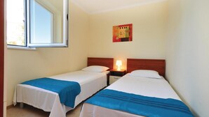Una habitación de hotel pequeña con dos camas individuales, una mesita de noche con lámpara y una ventana.