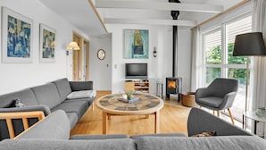 A modern living room with a sofa, armchairs, a coffee table, a TV, a fireplace, and artwork on the walls.