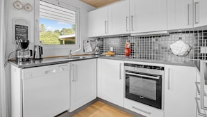A modern kitchen with white cabinets, a Siemens dishwasher, a Siemens oven, a coffee maker, and a window with blinds.