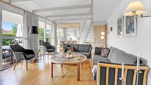 A modern living room with a sofa, chairs, a coffee table, and a dining area visible through large windows.