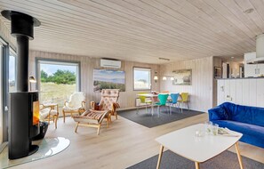 A spacious living area with a large fireplace, a blue sofa, and a dining table with colorful chairs. - Lovely home in Fanø with WiFi (Fanø)