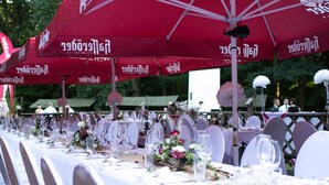 A banquet table set with white tablecloths, red umbrellas, and white chairs.