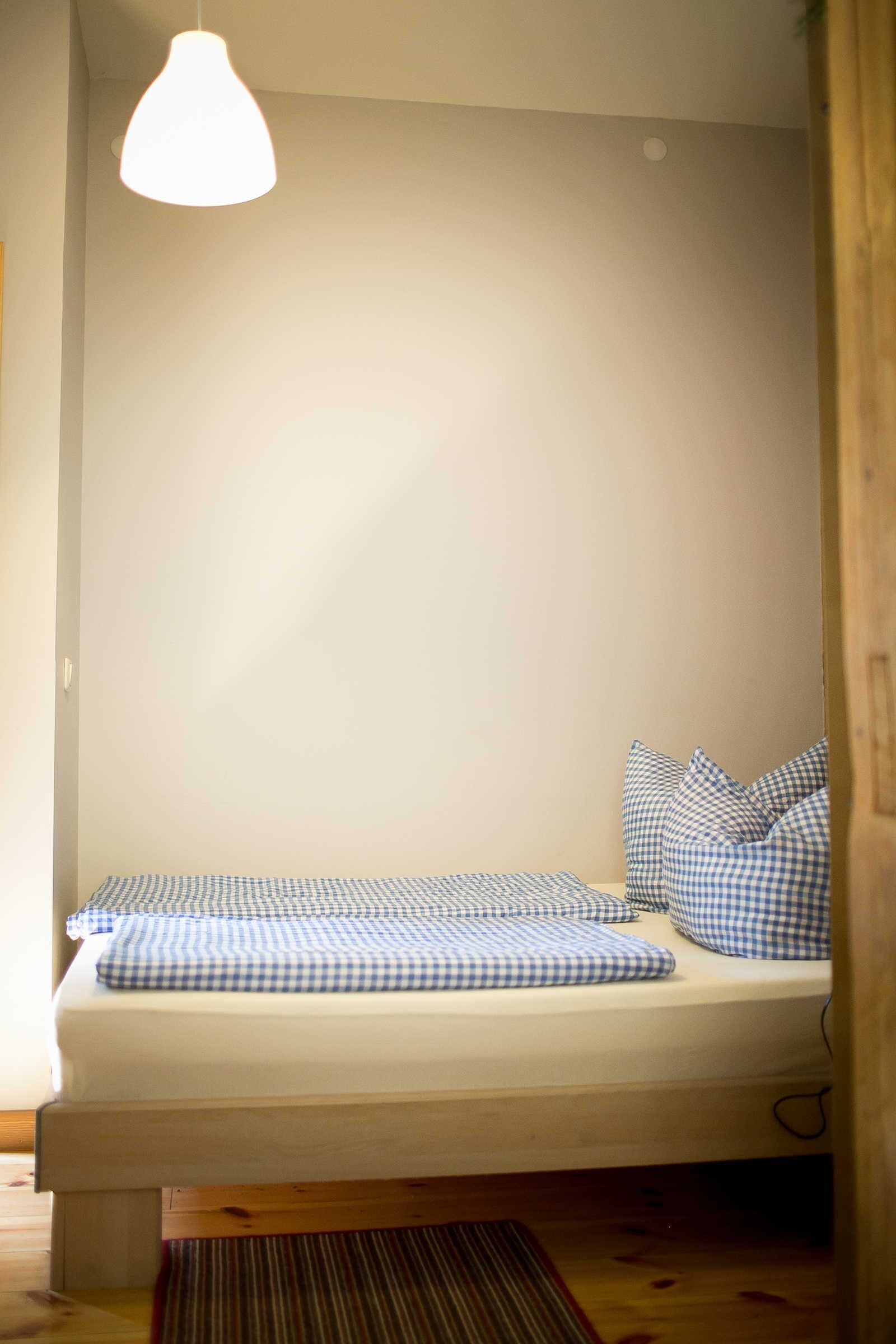 Ein Bett mit karierter Bettwäsche, eine Pendelleuchte und ein Holzboden.