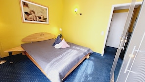 A room with a bed, a wall-mounted lamp, a framed picture, and a door. - (165) 2-room apartment - apartment house Sonnenresidenz I (Kühlungsborn)