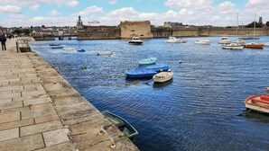 Un front marítim amb vaixells amarrats, una paret de pedra i un campanar al fons.