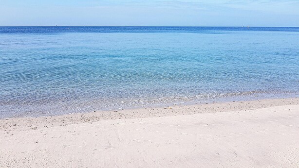 Una platja amb aigües poc profundes i clares i una riba sorrenca.