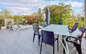 Eine Terrasse im Freien mit Tisch und Stühlen, umgeben von Grünpflanzen und einem Zaun.