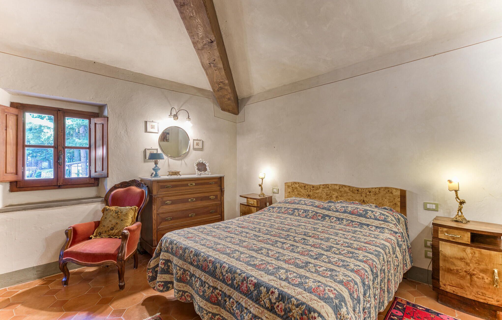 Un dormitorio con una cama de madera, una silla roja, un aparador y una ventana con cortinas.