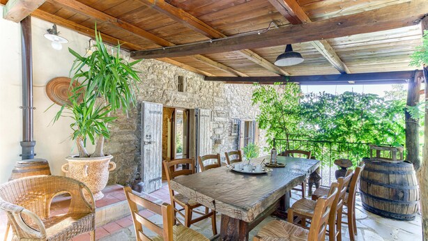 A rustic outdoor dining area with stone walls, wooden furniture, and potted plants.
