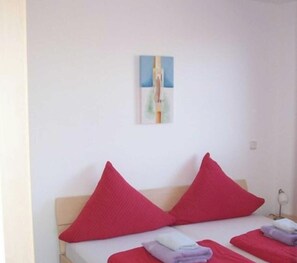 A bedroom with a bed, two red pillows, a painting on the wall, and a bedside lamp.
