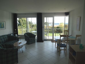 A living room with a sofa, chairs, a small table, and a balcony with a view.