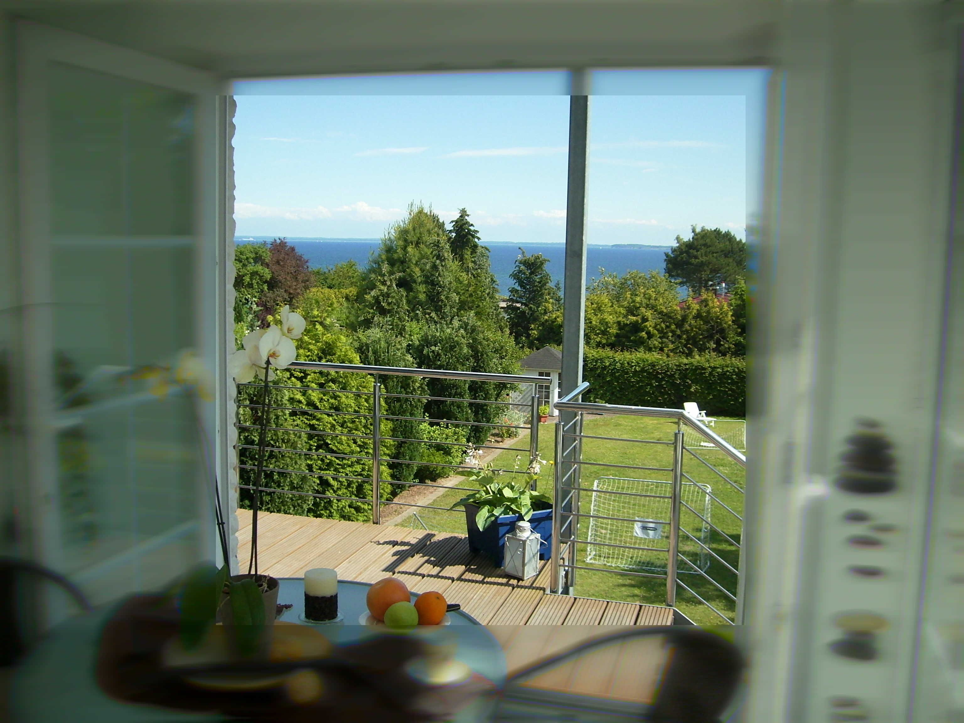 A balcony with a view of the sea, a railing, and a table with fruits and a candle.