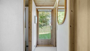 A narrow hallway with wooden walls and a door leading to a garden.