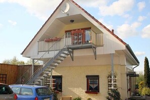 A two-story building with a balcony on the upper floor, a staircase leading to the balcony, and a car parked in front.